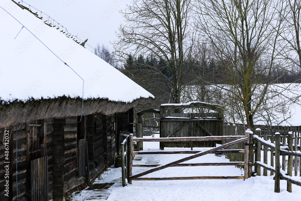 Winter Russian landscape. An old wooden hut, a log house with a thatched roof. Abandoned Russian village covered in snow. Log house with a barn with a wooden wicker fence. Winter Russian landscape. An old wooden hut, a log house with a thatched roof. Abandoned Russian village covered in snow. Log house with a barn with a wooden wicker fence.