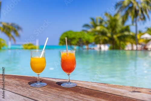 Colorful cocktails served on luxury tropical resort hotel in Maldives. Poolside with blurred palm trees and loungers and sunlight. Bright sunny infinity pool under blue sky. Tropical beach lifestyle