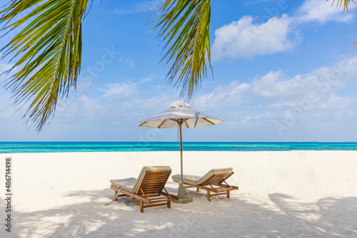 Fantastic beach scene with two sun beds loungers under umbrella and palm leaves. Tropical nature paradise island shore coast sea view, horizon under calm sky. Idyllic summer couple beach landscape © icemanphotos