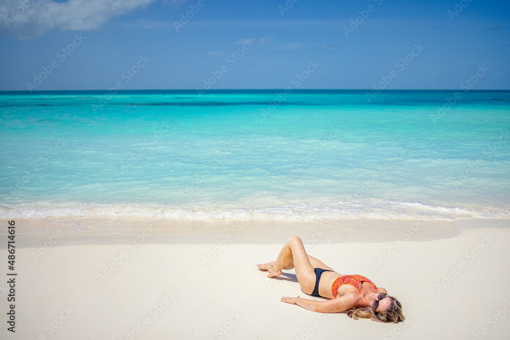 Fashion woman portrait in bikini on tropical beach. Relaxing summer mood, calm waves on sandy beach, exotic tropical island landscape with woman relaxing in the sand, sunglasses and sexy swimwear Fashion woman portrait in bikini on tropical beach. Relaxing summer mood, calm waves on sandy beach, exotic tropical island landscape with woman relaxing in the sand, sunglasses and sexy swimwear