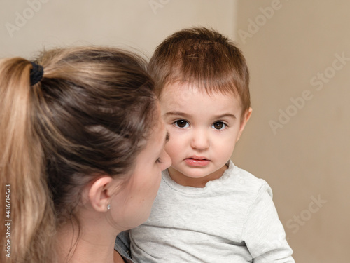 Portrait of a sad baby. Mother holding a boy in her arms. Tense look on the baby's face.