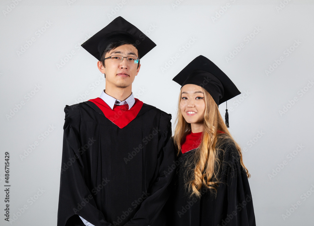 Graduates couple in gowns posing together on white background Graduates couple in gowns posing together on white background