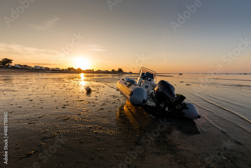 Bateau semi-rigide pour la pêche de loisir côtière posé sur le sable à marée basse au soleil couchant. Le Vieil à Noirmoutier photo