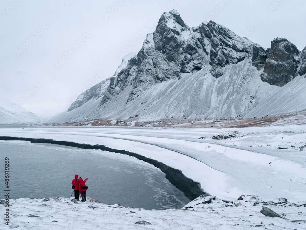 Two people in red coats at Hvalnes in winter. Mount Eystrahorn in background. East Iceland.