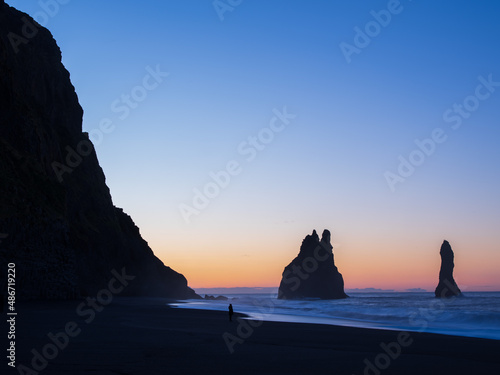 Reynisfjara black sand beach before sunrise in winter. Person standiong near the surf. South Iceland.