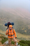 A man climbs a mountain in the fog, a man carries a backpack on his back.