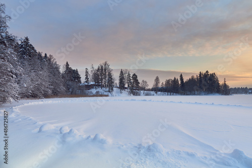 Winter sunset near the Finnish Tuusula lake: shore, snow on ice as oval, nature of northern Europe, coniferous forest.