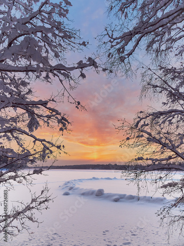 Winter sunset near the Finnish Tuusula lake: shore, snow on ice as oval, nature of northern Europe, framed.