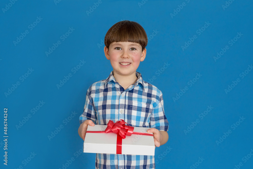 The boy with a gift smiles on a blue background. Mothers Day. March 8. The boy gives a gift. The boy with a gift smiles on a blue background. Mothers Day. March 8. The boy gives a gift.