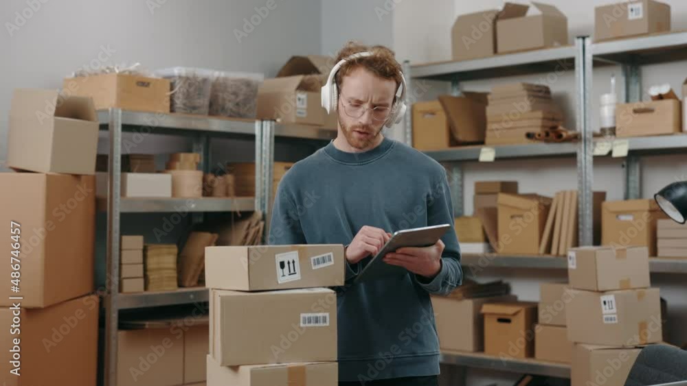Waist up portrait view of the caucasian man typing something on the tablet while checking information about parcel and preparing sending it to the client. Small business concept. Waist up portrait view of the caucasian man typing something on the tablet while checking information about parcel and preparing sending it to the client. Small business concept.