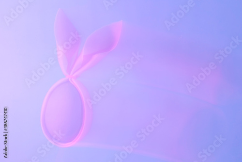 Abstract frame-washed background of neon holographic purple color trek of pink egg with rabbit ears. Creative handmade concept. © Ekaterina