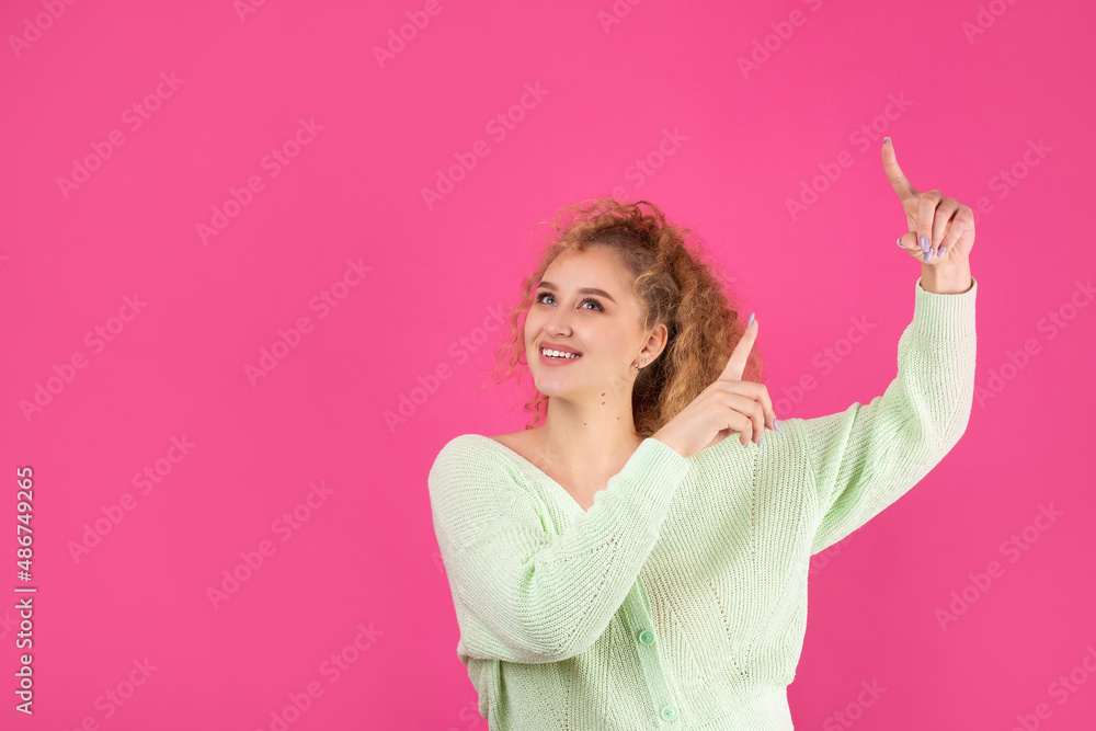 Fototapeta premium A young girl with curly hair points with a gesture on a studio background.
