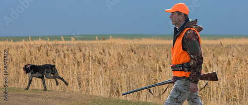 Hunter man in camouflage with a gun during the hunt in search of wild birds or game. Autumn hunting season.