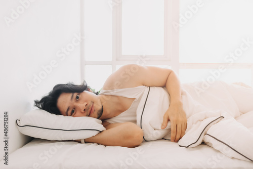 Asian man just wake up in a happy morning in bright white bedroom.