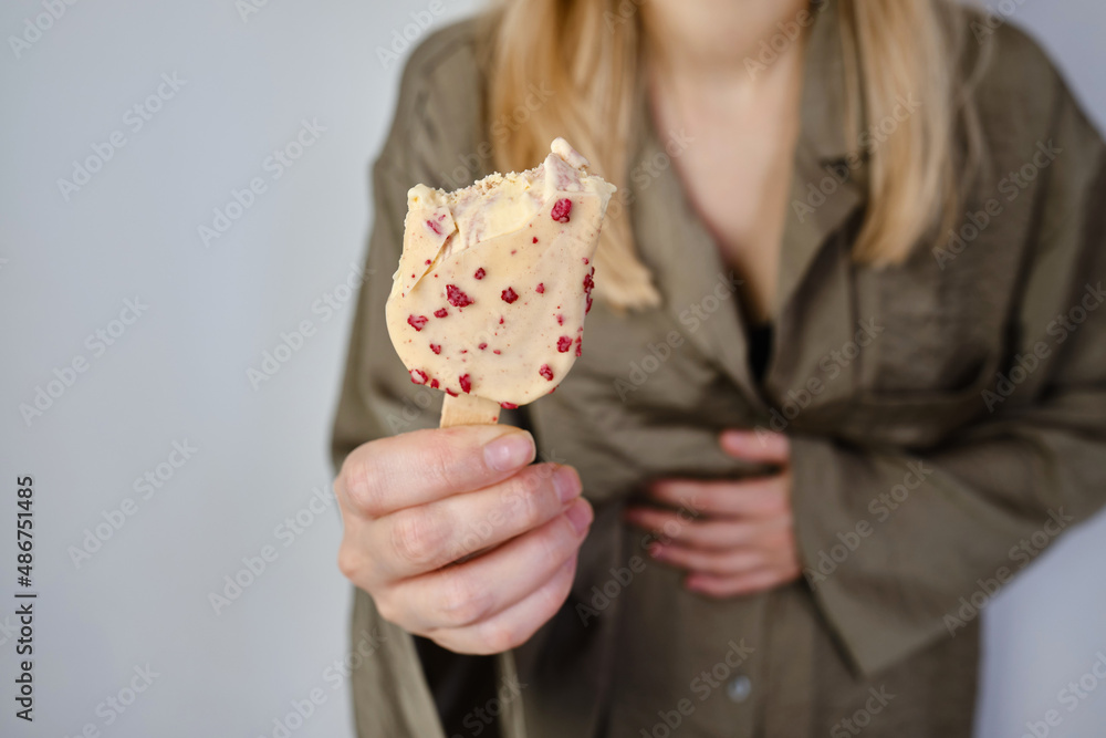 The girl eats ice cream and holds her stomach. Delicious sweet dessert. Ice cream in white chocolate close-up. Fast food and proper nutrition for the body The girl eats ice cream and holds her stomach. Delicious sweet dessert. Ice cream in white chocolate close-up. Fast food and proper nutrition for the body