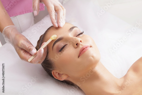 Beautician is removing hair from beautiful female face with hot wax. Woman has a beauty treament procedure. Depilation, epilation, skin and health care concepts.