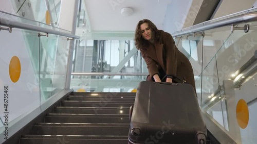 Slow motion footage of young elegant woman carrying heavy suitcase up the stairs at the airport. The concept of traveling with heavy luggage, being late for a flight