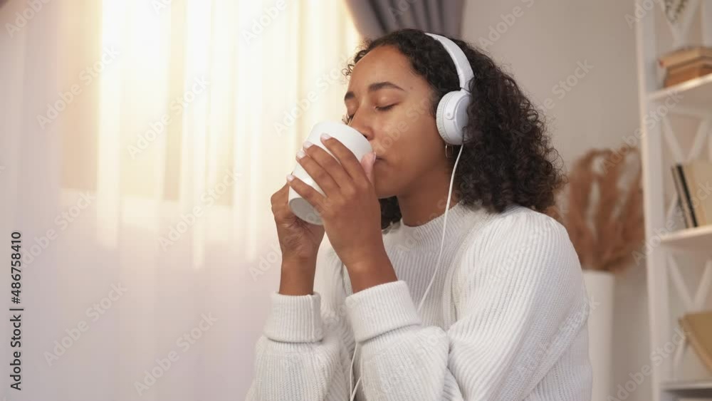Coffee relax. Weekend indoors. Home leisure. Satisfied peaceful dreamy woman drinking morning mug of tea listening music in earphones enjoying Sunday cozy rest. Coffee relax. Weekend indoors. Home leisure. Satisfied peaceful dreamy woman drinking morning mug of tea listening music in earphones enjoying Sunday cozy rest.