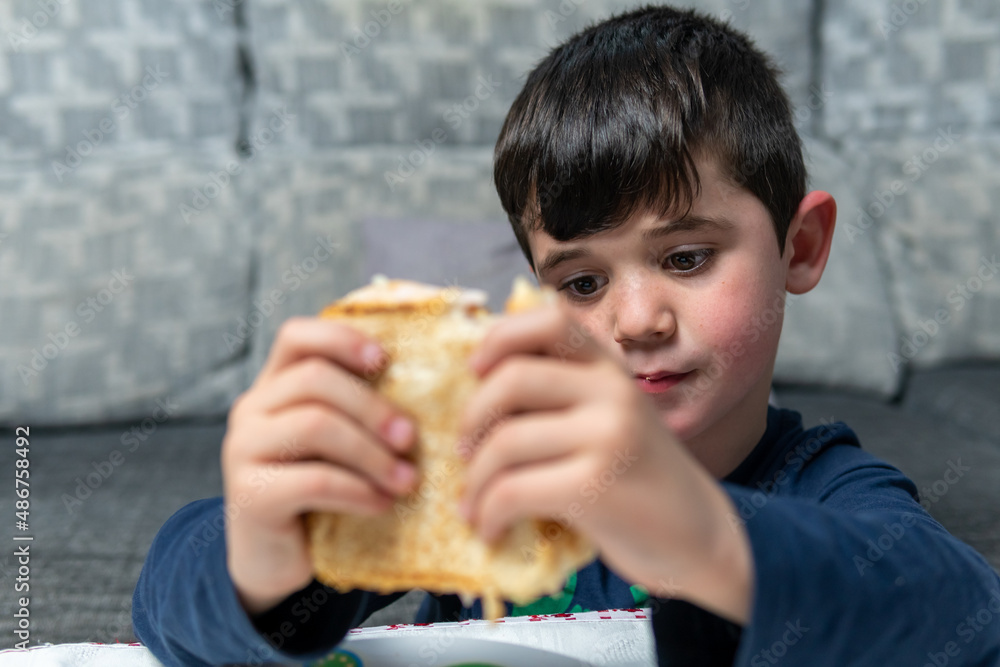 Young boy eating a ham and cheese sandwich for snack at his grandmother's house. After doing homework it's time to have a snack. Young boy eating a ham and cheese sandwich for snack at his grandmother's house. After doing homework it's time to have a snack.