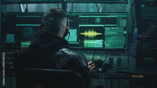 Young man with headset stealing private data from victim by making call from high tech base with computers