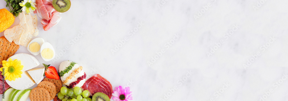 Spring or Easter charcuterie corner border against a white marble banner background. Top down view. Assortment of cheese, meat and fruit appetizers. Copy space.