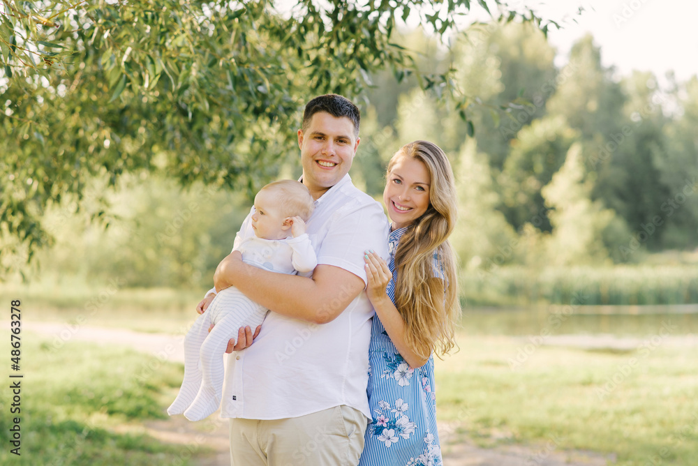 Obraz premium A European family in the park on a summer day. Happy and smiling mom, dad and little son in their arms. Dad plus size