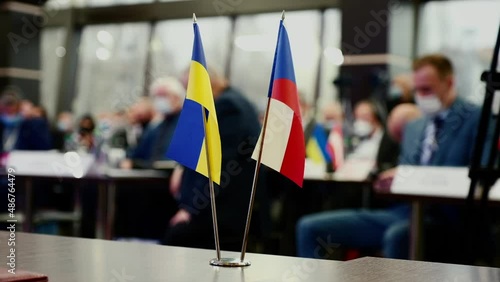 Ukrainian and Check Republic flags on desk on foreground. Blurred view of people sitting at tables at international conference behind banners closeup