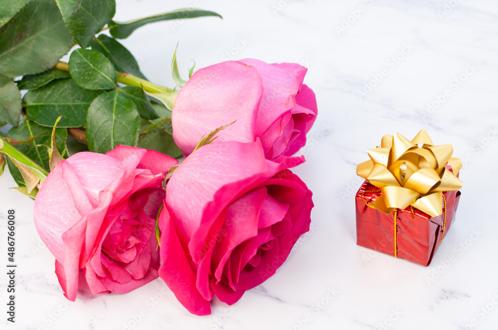Fototapeta premium A simple arrangement with a flower and a heart shape decoration. Rose and gift box on marble background.