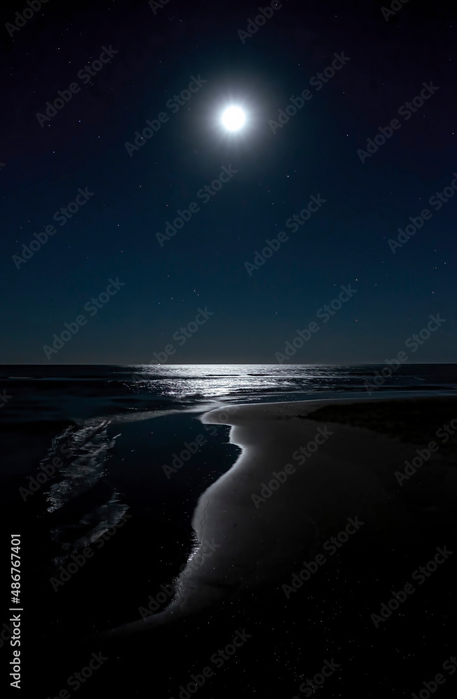night image of a beach with the moon in the starry sky reflecting on the water of the seashore, painting a cave of light, Isla Canela, Huelva Spain, vertical