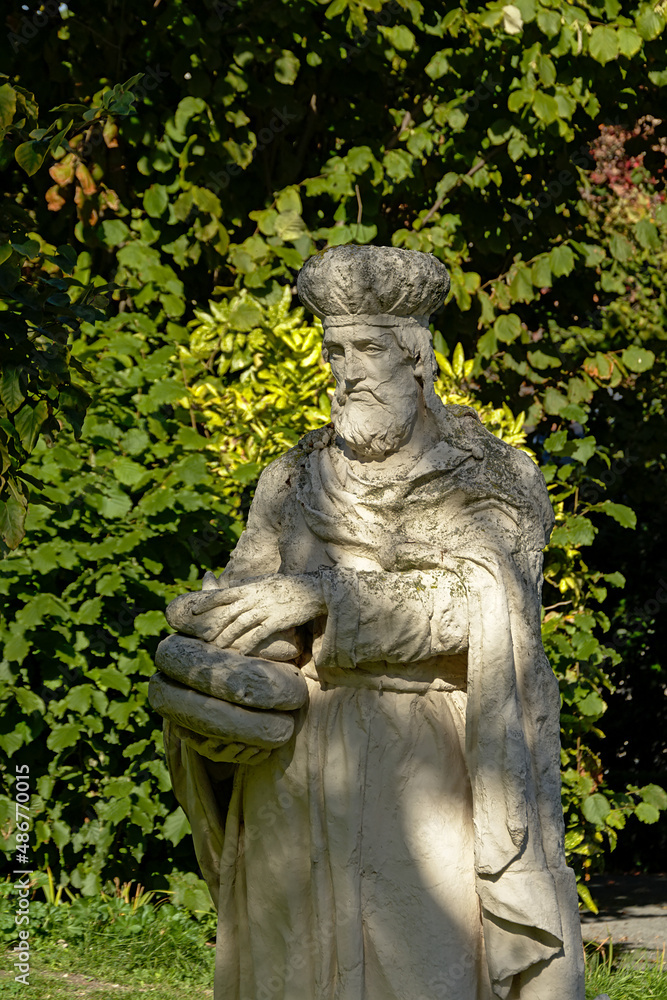 Stone sculpture of a saint holding bread, selective focus with green shurbs in the background, found in the beguinage of Antwerp, Flanders,s Belgium 
