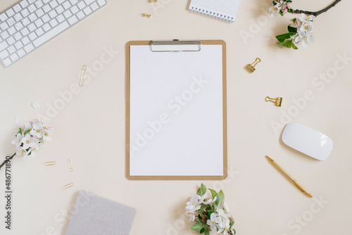 Stylized feminine or blogger desk, office desk. Workplace, white flowers of an apple tree, notebook, pen, paper clips and a tablet with a blank white sheet of paper on a beige background