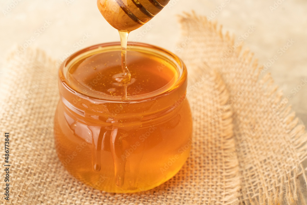 Golden organic honey in a jar with a wooden stick closeup. Concept of healthy nutrition organic food. Background for beekeepers for honey products Golden organic honey in a jar with a wooden stick closeup. Concept of healthy nutrition organic food. Background for beekeepers for honey products