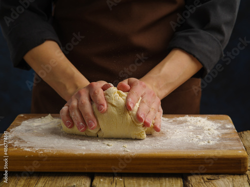 The chef's hands are kneading the dough on a wooden board. Macro shot. Preparation of dough products. Recipes for pizza, bread, pasta, pastry. Home cooking, restaurant, hotel, bakery.