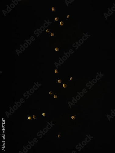 Grains of black pepper in a frozen flight on a black background. There are no people in the photo. Spices, seasonings, ingredient for various spicy dishes. Advertising, restaurant, cafe.