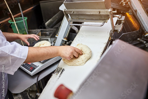 Hands of woman confectioner in uniform weighing dough for pastry at the bakery manufacturing