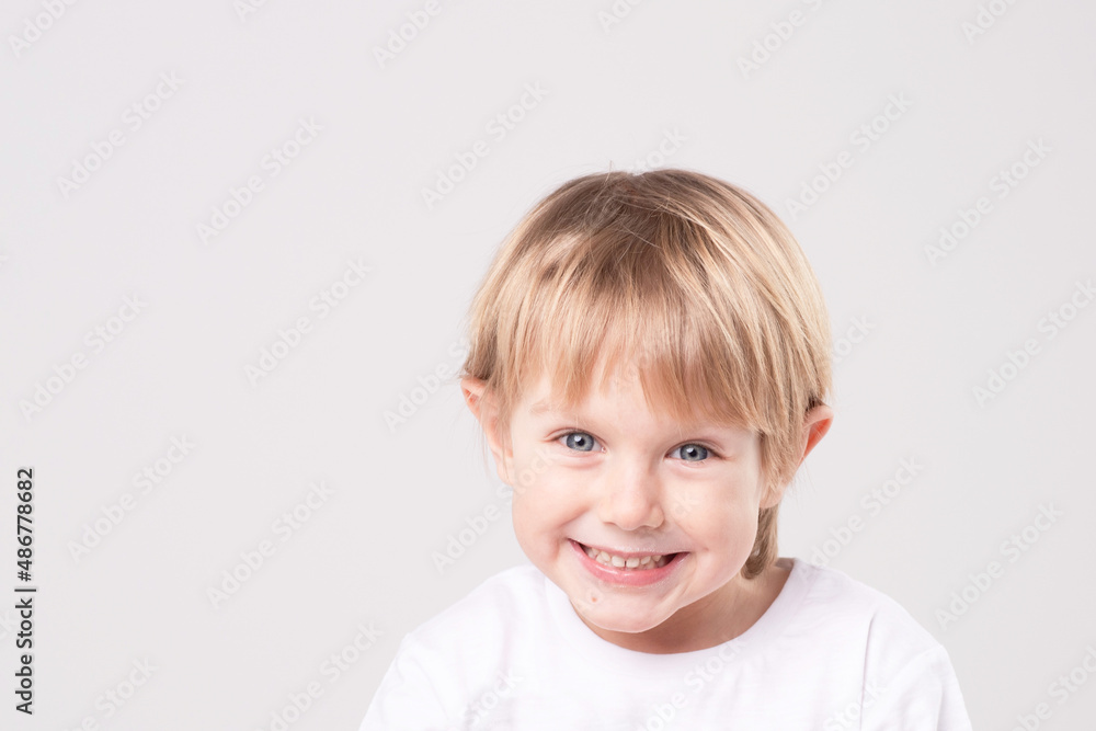 Beautiful blond child posing smiling on studio background. Emotional face. Dental smile. Cheerful boy 5-6 years old. White T-shirt. Eye contact. Copy space. Beautiful blond child posing smiling on studio background. Emotional face. Dental smile. Cheerful boy 5-6 years old. White T-shirt. Eye contact. Copy space.