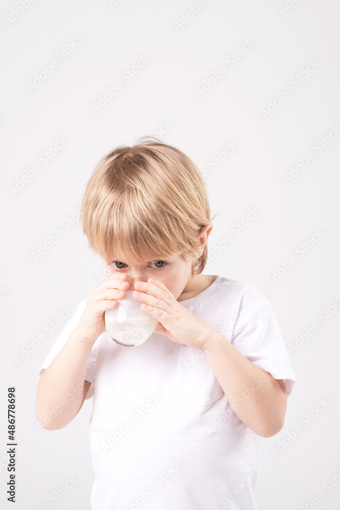 Caucasian child drinks milk from the glass. White studio background