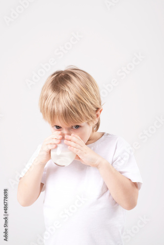 Caucasian child drinks milk from the glass. White studio background. Vitamins, calcium, milk teeth, dairy products, healthy food, advertising concept. Copy space.