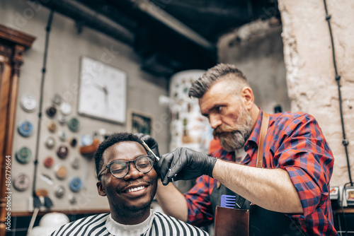 Young African man visiting hairstylist in barber shop. Professional hairdresser cut hair with scissors.