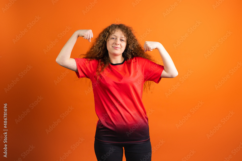 Redhead fan football woman in red t-shirt showing her muscles and supporting her favourite football team on the championship. Redhead fan football woman in red t-shirt showing her muscles and supporting her favourite football team on the championship.