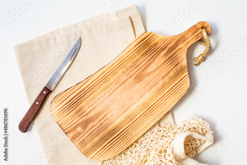A cutting wooden board, a knife and linen towel are on a white background. Copy space. Thematic background for the recipe of the dish. Top view.