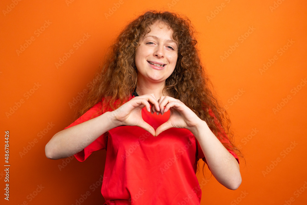 Picture of a smiling woman in soccer football uniform red color showing heart sign using two hands, football support concept. Picture of a smiling woman in soccer football uniform red color showing heart sign using two hands, football support concept.