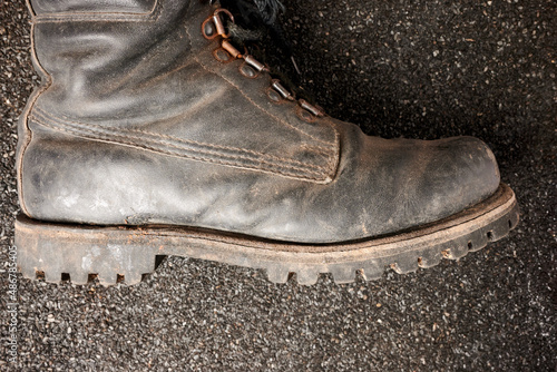 Old man boot on ruberoid mineral surface. Military boot for male. Single leather black boot. Black textured background. Usual footwear for men. Foot covering leather protection. Army boot. photo