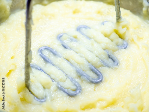 Metal potato masher in freshly made mashed potatoes. Selective focus. Pestle for making mashed potatoes close-up. photo