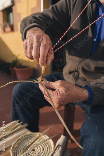 vertical photo of a craftsman working a rope with palm leaf. craft piece