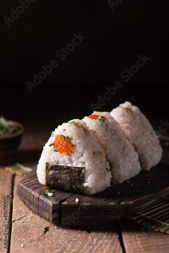 Japanese traditional snack rice balls triangle onigiri with raw salmon and red caviar on a dark wooden board in rustic style