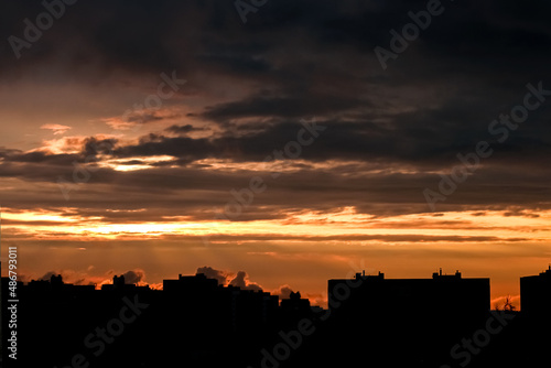 The black silhouette of the city at sunset. Yellow sky with clouds and rays of light breaking through them