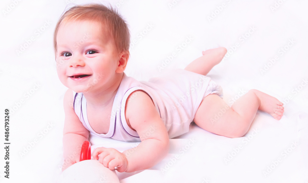 A caucasian baby boy lies in a white bodysuit with a toy on a white background A caucasian baby boy lies in a white bodysuit with a toy on a white background