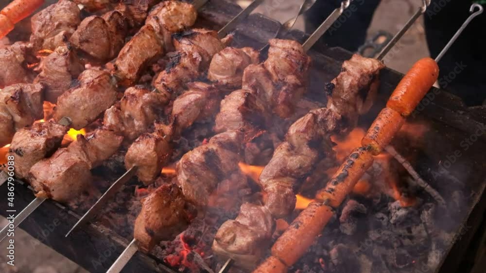 a man roasts meat on a fire. Close-up of hands and shish kebab. Cooking pork neck on the grill. Roasted carrots. Fatty food, festive food of the CIS countries. May 1, labor day. Not vegan food. a man roasts meat on a fire. Close-up of hands and shish kebab. Cooking pork neck on the grill. Roasted carrots. Fatty food, festive food of the CIS countries. May 1, labor day. Not vegan food.