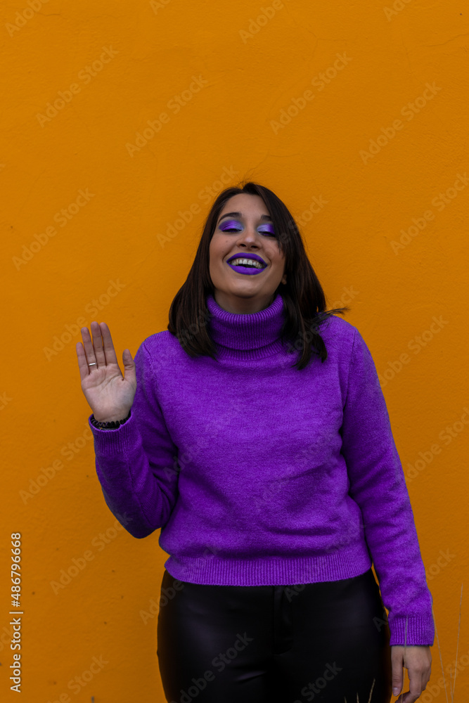 vertical portrait of a happy smiling woman dressed in purple makeup waving to the camera on a yellow background vertical portrait of a happy smiling woman dressed in purple makeup waving to the camera on a yellow background
